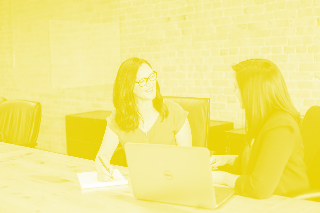 Two Business Women Talking while one takes notes
